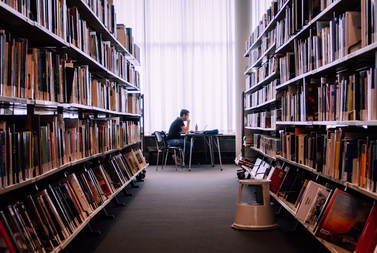 services-01 A person studies alone in a peaceful library filled with books, capturing a quiet moment of learning.