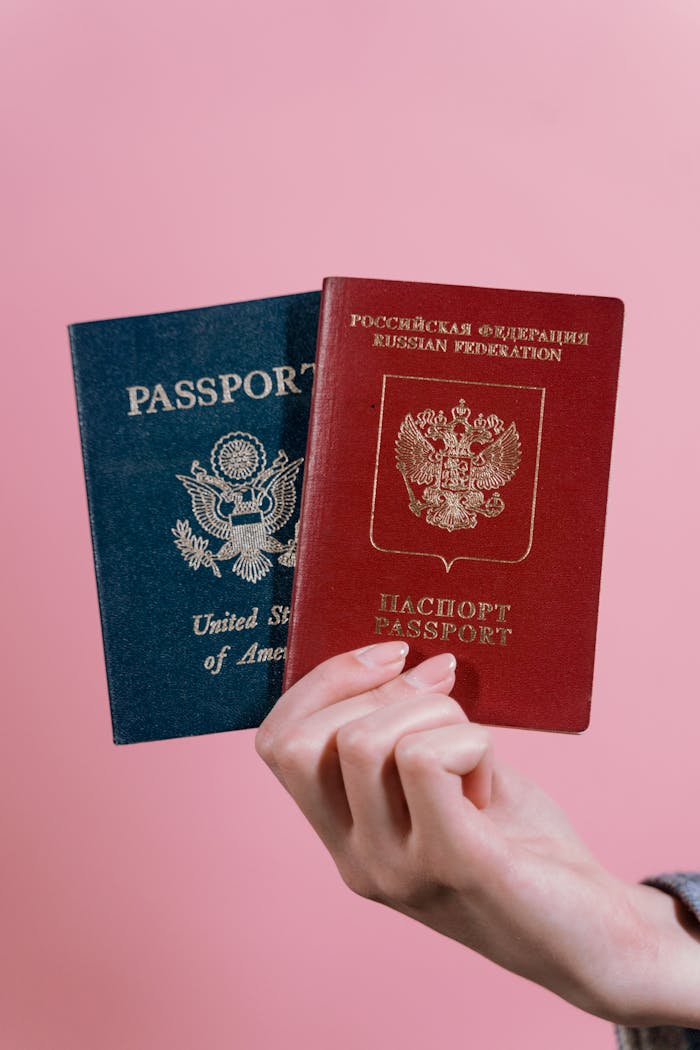 hero-img-02 A hand holding US and Russian passports against a pink background.
